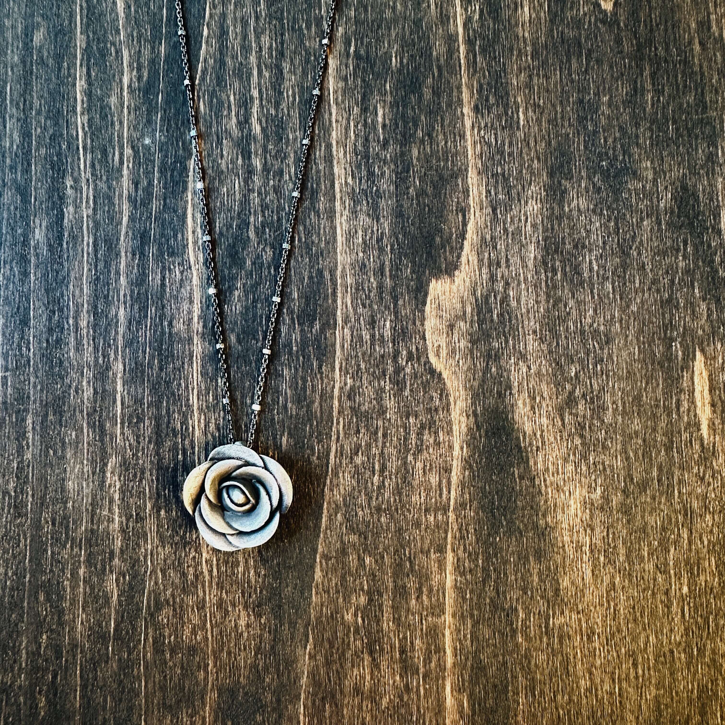 Close-up detail of handsculpted sterling silver rose pendant on wood — each petal shaped by hand, one of a kind artisan rose necklace by Jester Swink