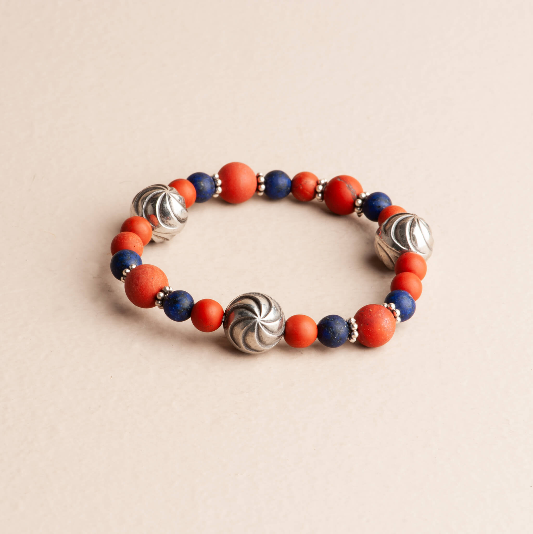 Handmade 7-inch stretch bracelet featuring alternating red Jasper beads and small deep blue Lapis Lazuli beads, separated by large, ridged sterling silver swirl beads.