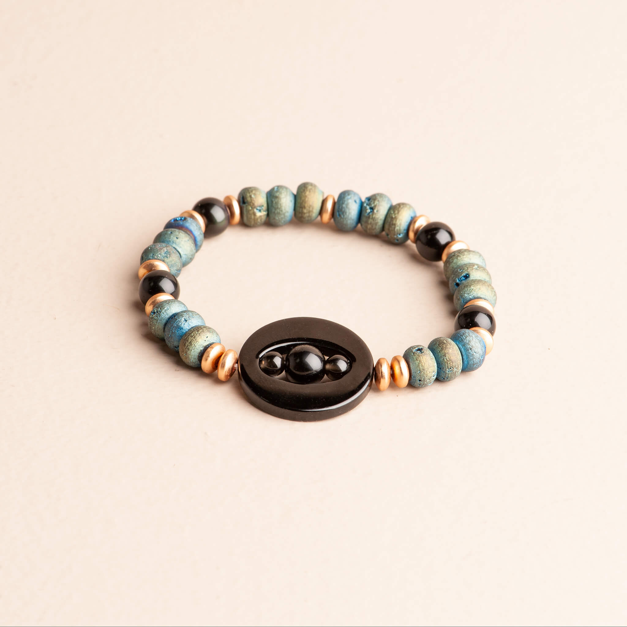 Close-up of a stretch bracelet featuring a large black onyx focal bead, textured blue druzy quartz, and rose gold plated hematite spacers.