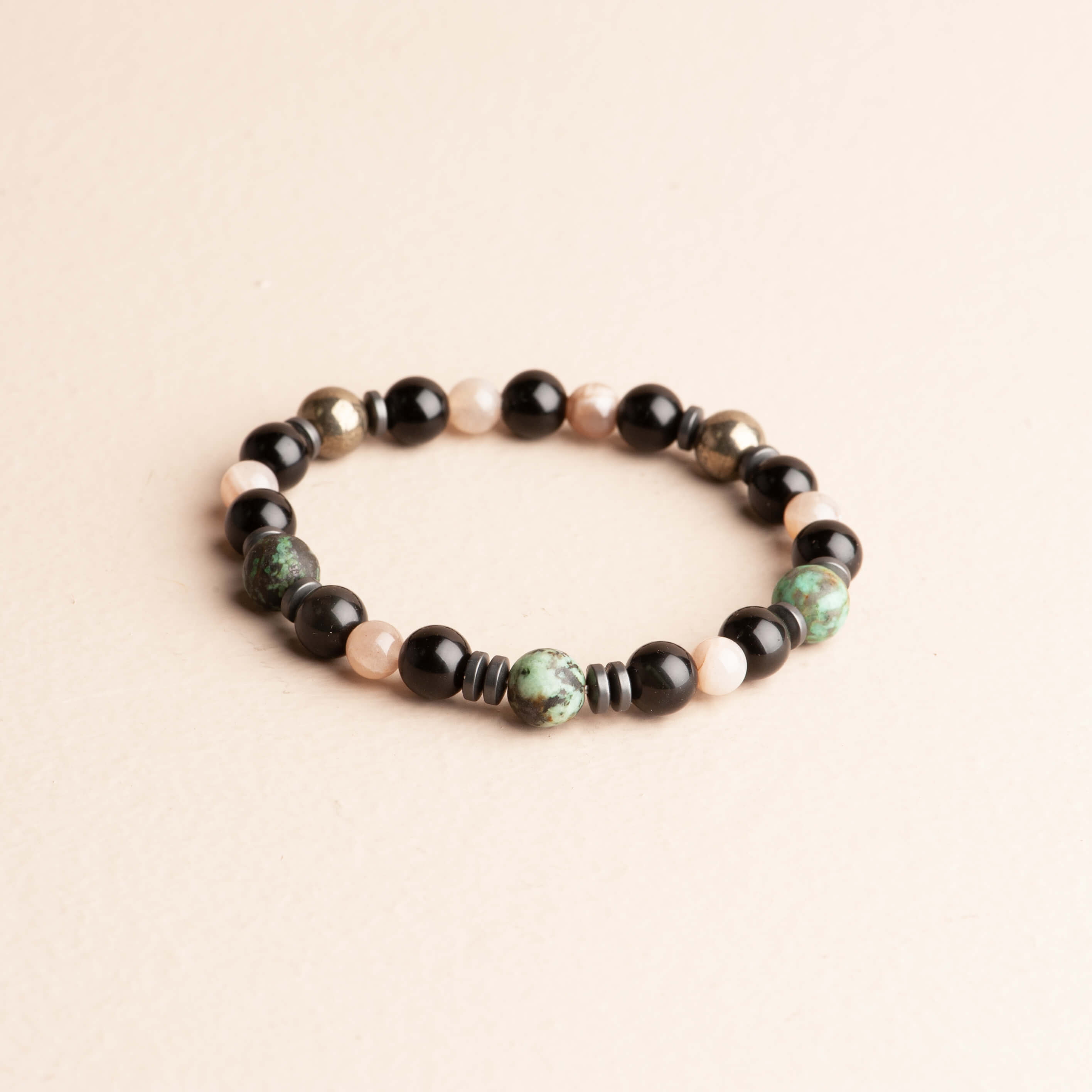 Sleek 7-inch stretch bracelet featuring black obsidian, earthy green African turquoise, soft peach moonstone, **pyrite accent beads**, and dark grey hematite spacer beads.