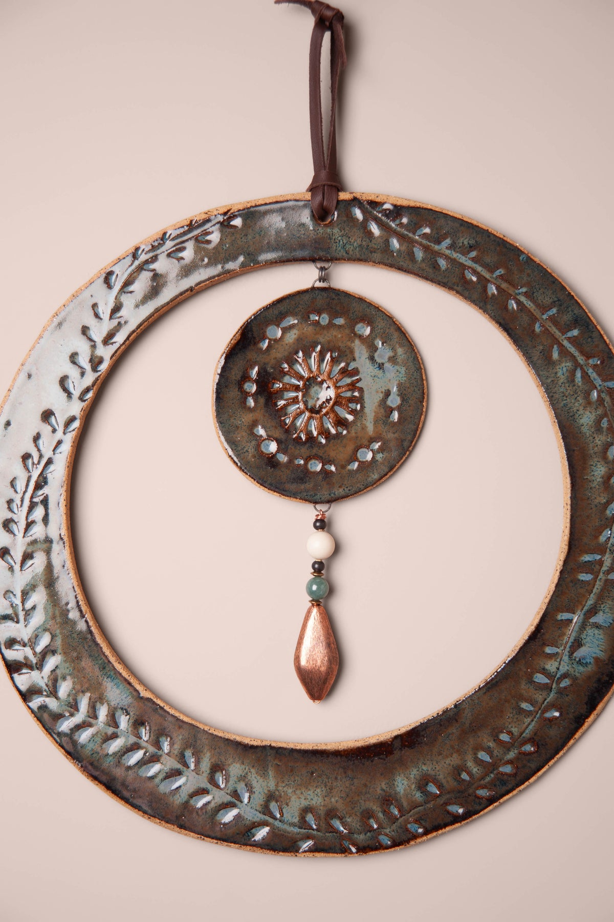 Detail of the hand pressed sun and vines on a large handmade round ceramic wall hanging, kiln fired by Jester Swink, Santa Cruz Mountains California