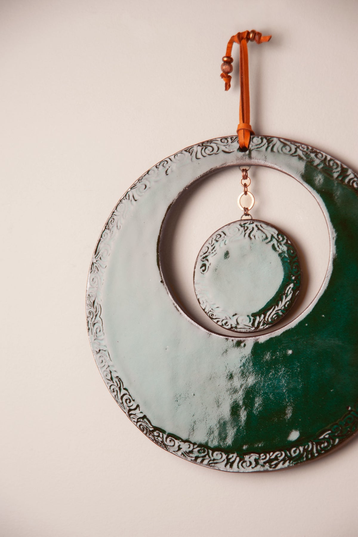 Detail of the textured rim and hanging disc on a large handmade round ceramic wall hanging in Emerald glaze, kiln fired by Jester Swink, Santa Cruz Mountains California