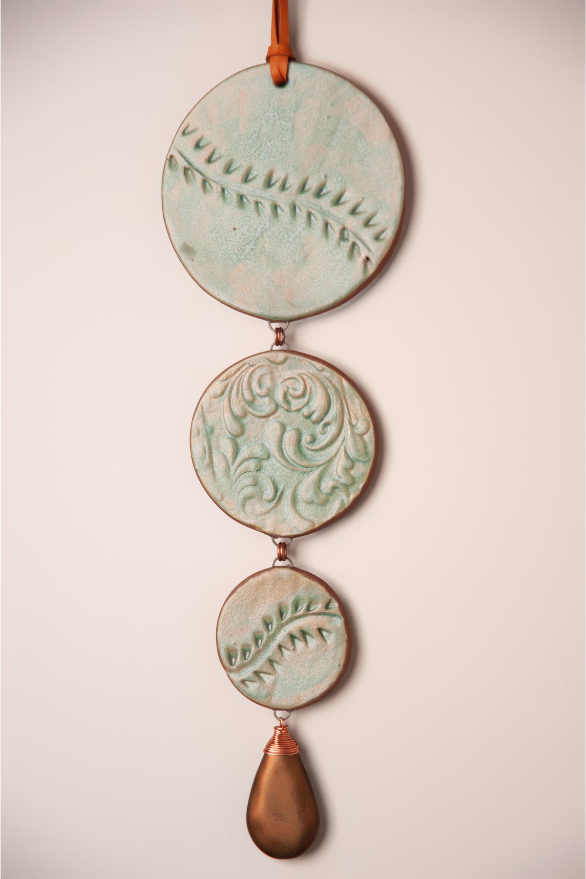 Detail of pressed vine patterns on the stepped discs of a large handmade tiered ceramic wall hanging, kiln fired by Jester Swink, Santa Cruz Mountains California