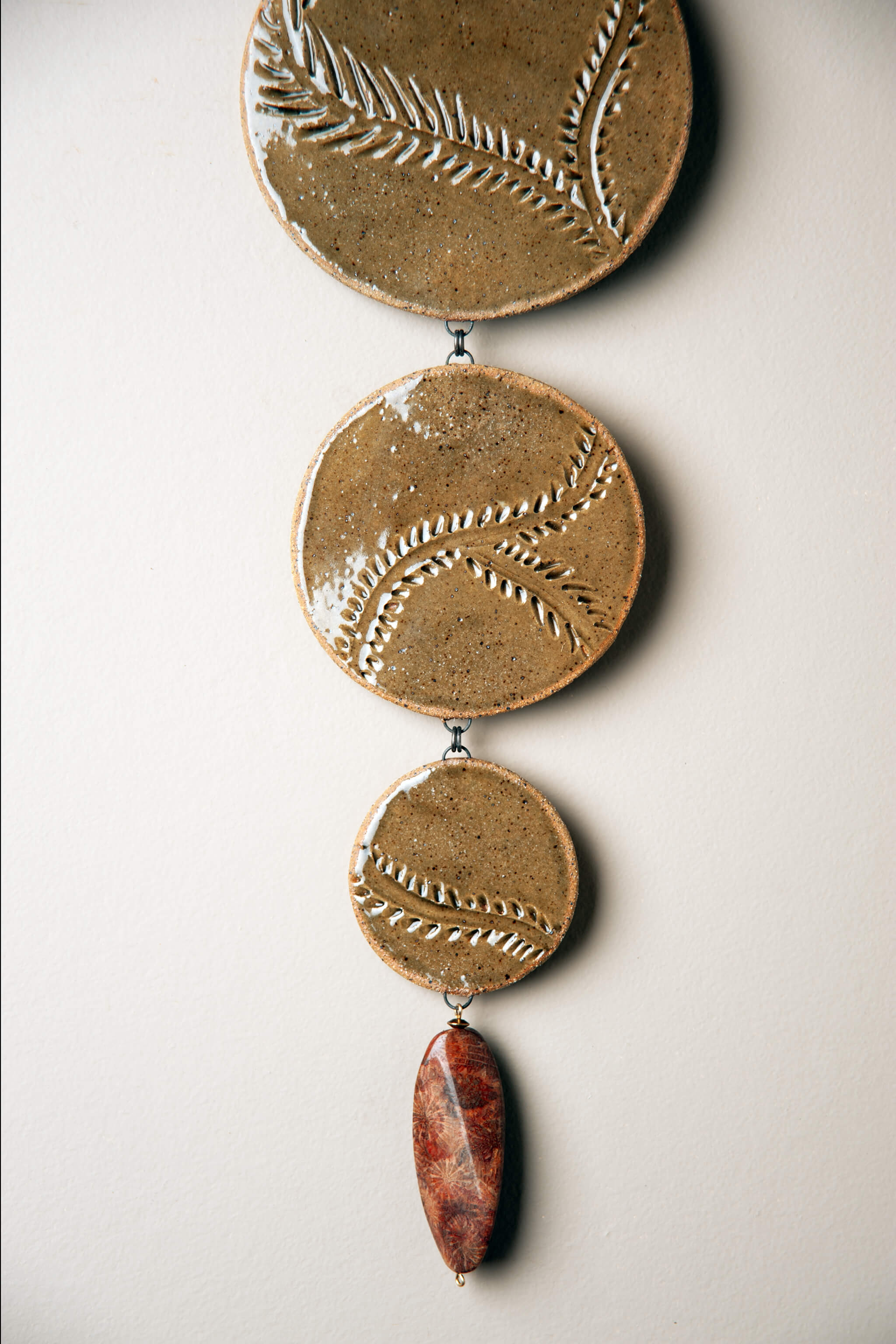 Detail of hand carved vine and leaf pattern with olive green glaze on handmade cascading ceramic wall hanging by Jester Swink, Santa Cruz Mountains California