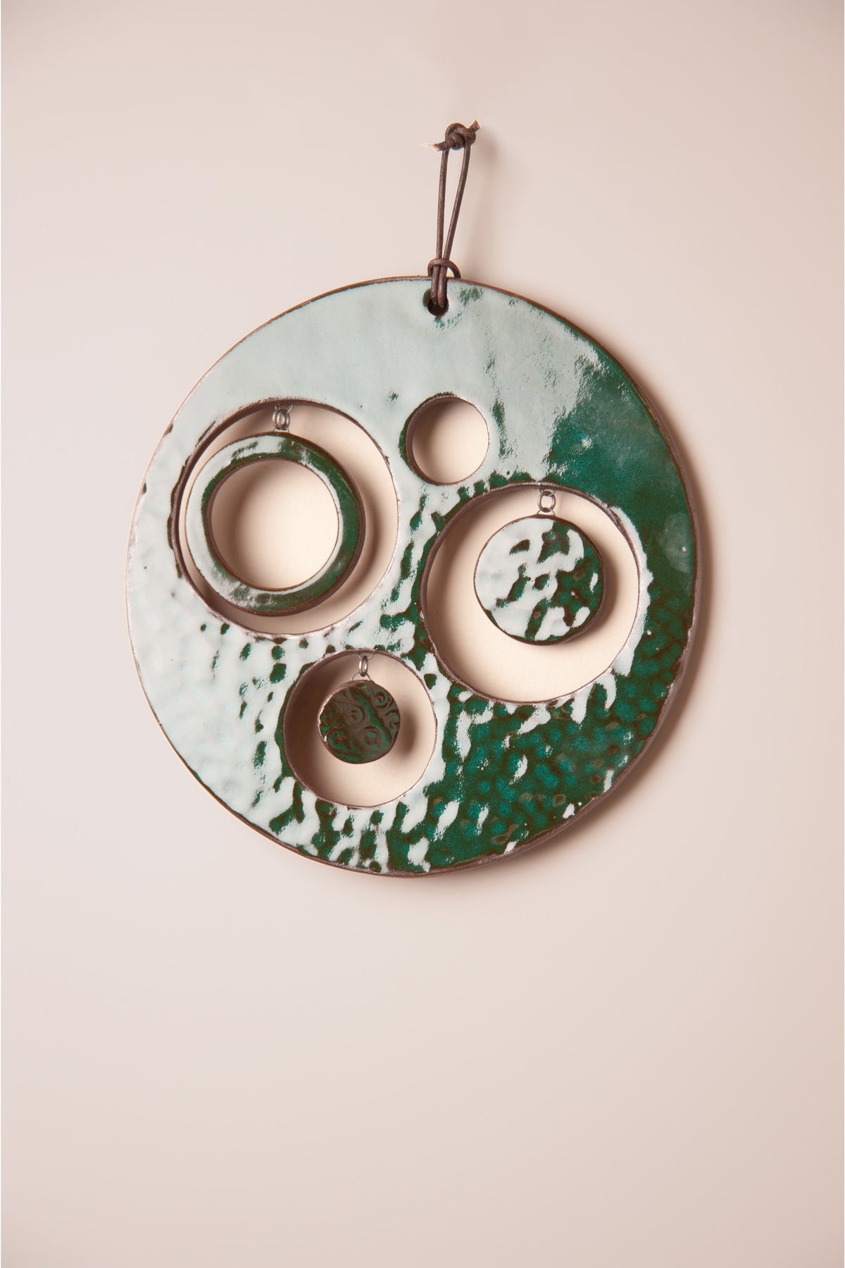Detail of the hammered Emerald glaze and hanging moons on a medium handmade round ceramic wall hanging, kiln fired by Jester Swink, Santa Cruz Mountains California
