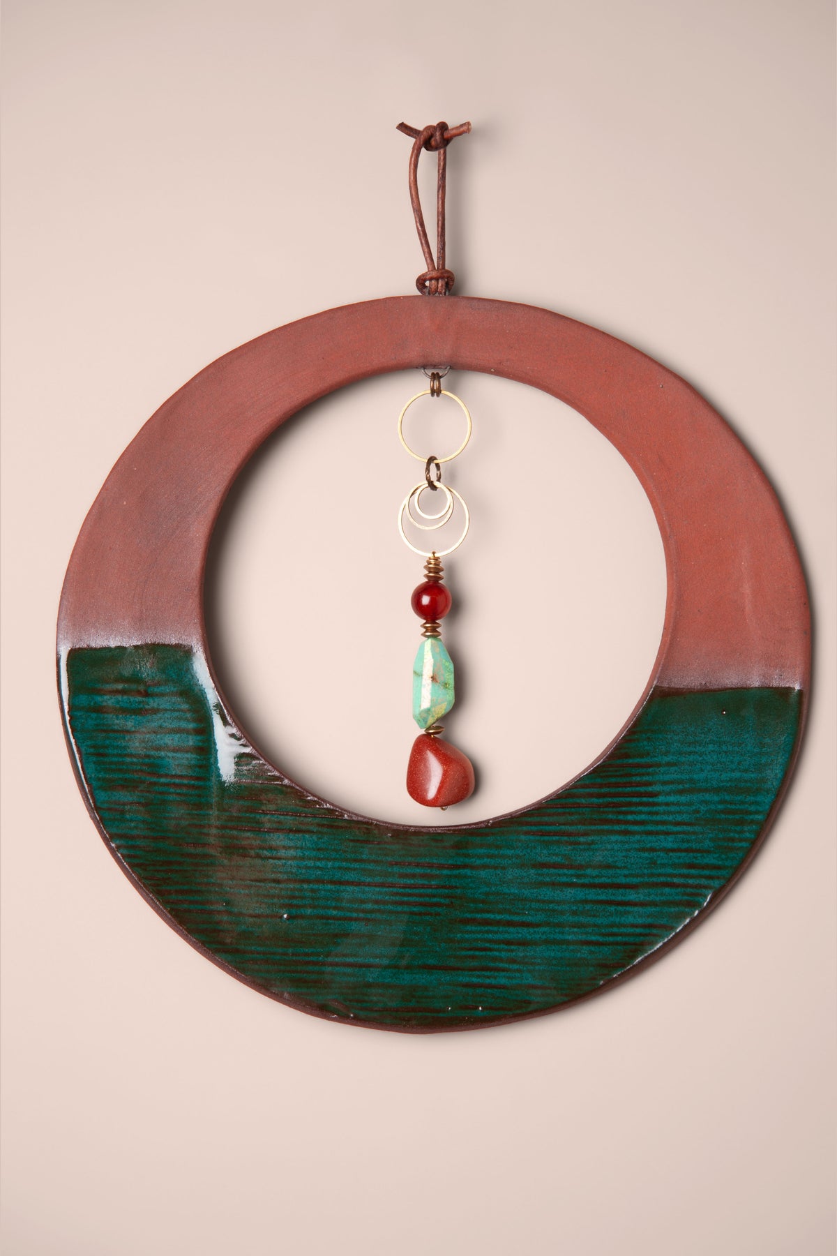 Detail of the terracotta and emerald glaze with the stone dangle on a medium handmade round ceramic wall hanging, kiln fired by Jester Swink, Santa Cruz Mountains California