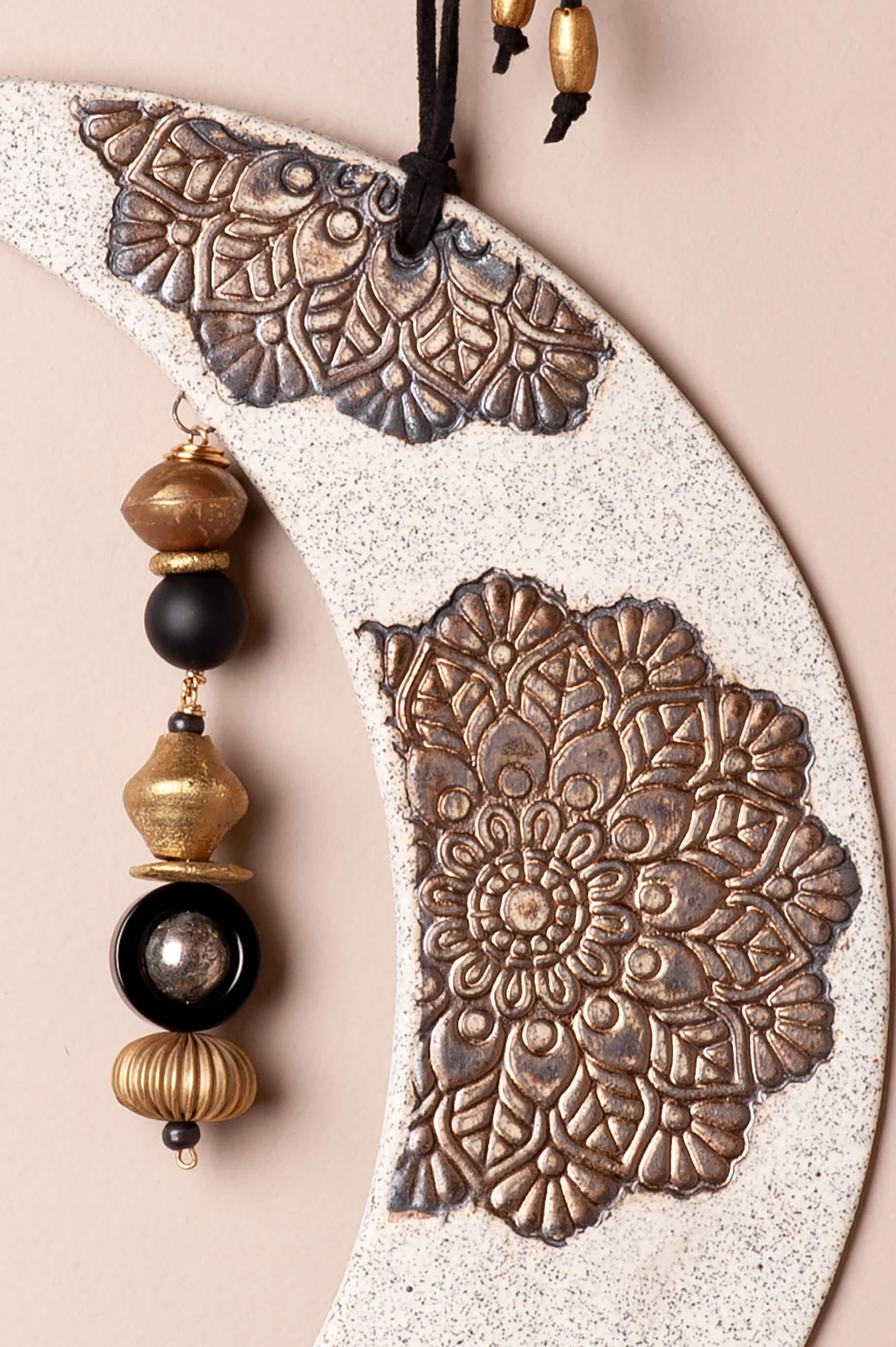 Close-up of handmade ceramic moon mandala wall hanging with brass, bronze, pyrite, and onyx details