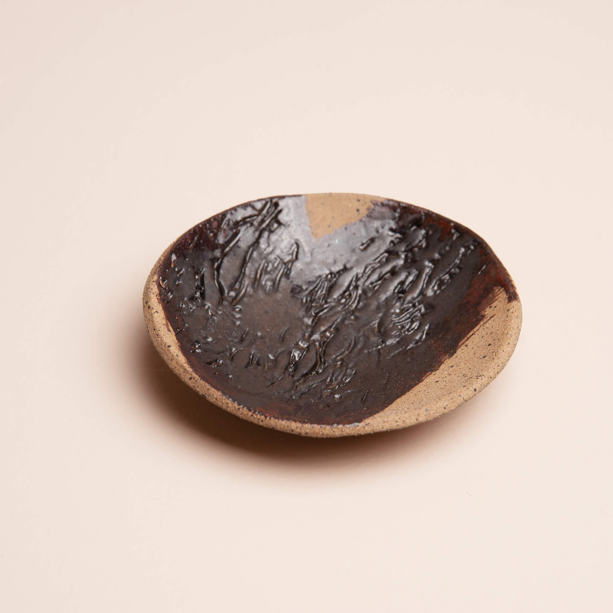 Angled view of handmade ceramic Sierra Banksia ring dish showing depth and organic shape, deep brown copper glaze on speckled sierra clay, by Jester Swink