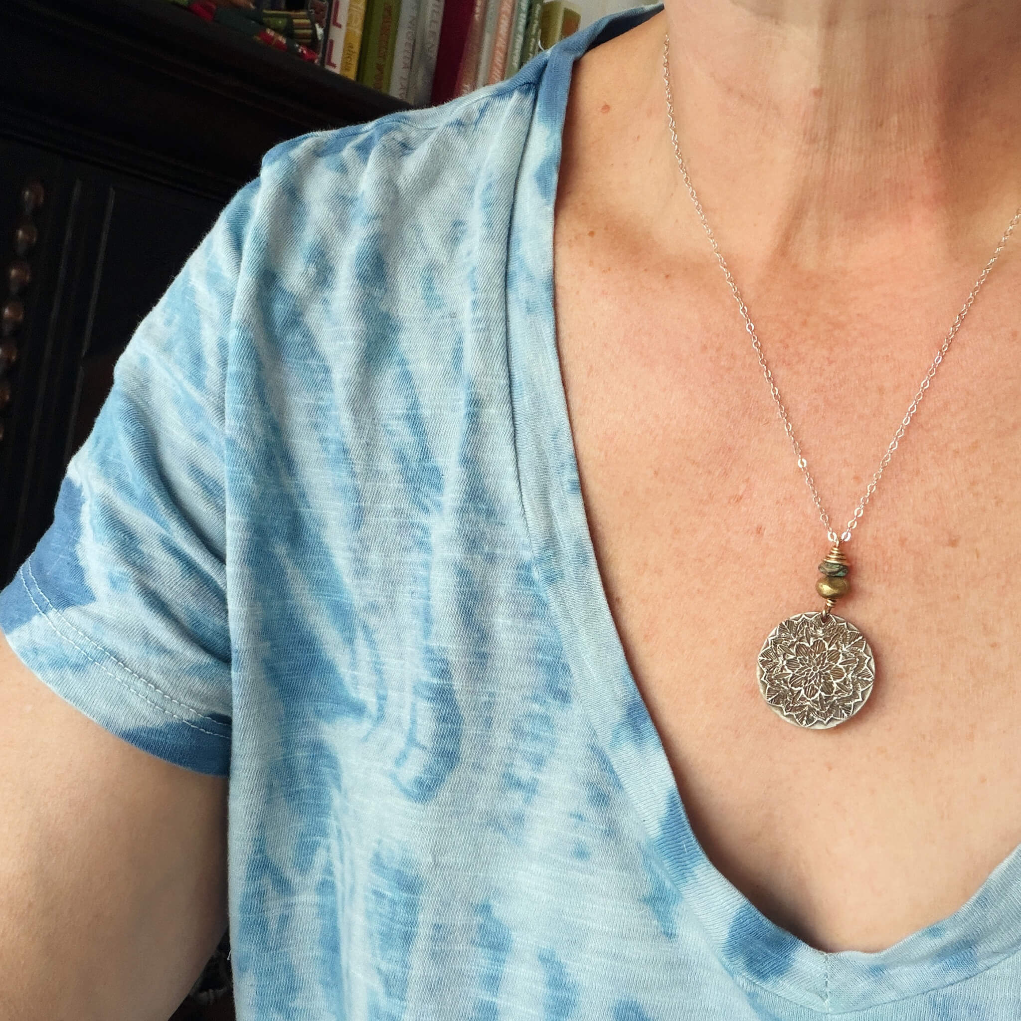 Person wearing a blue tie-dye shirt with a necklace featuring a circular pendant.