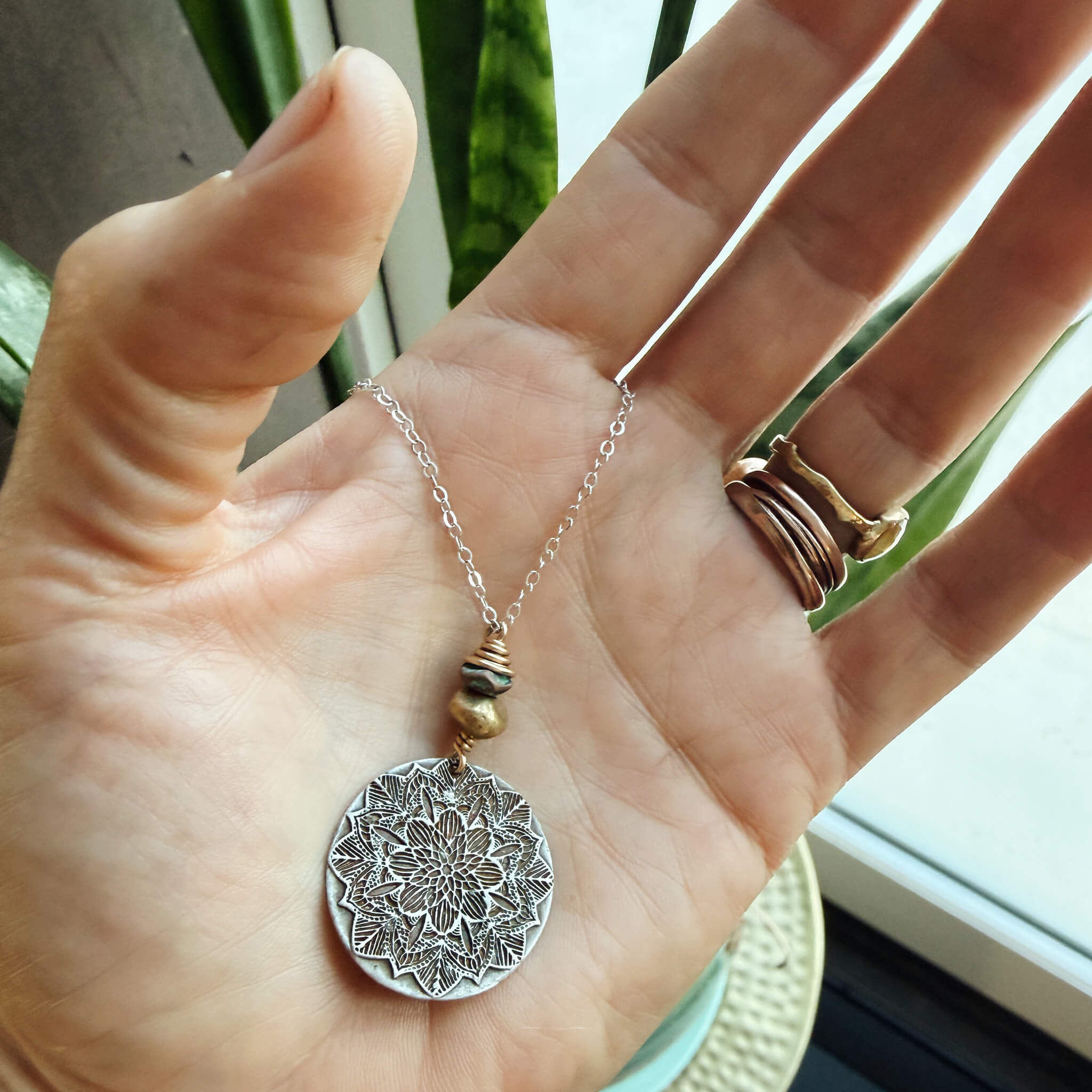 Close-up of handcrafted sterling silver mandala pendant with turquoise patina brass and 14K gold-fill wire wrapping — artisan mandala jewelry by Jester Swink