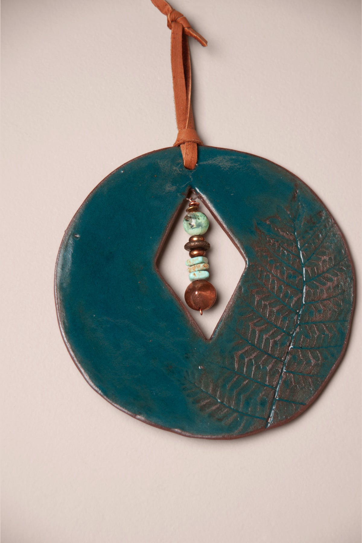 Detail of the fern impression in Emerald glaze on a small handmade round ceramic wall hanging, kiln fired by Jester Swink, Santa Cruz Mountains California