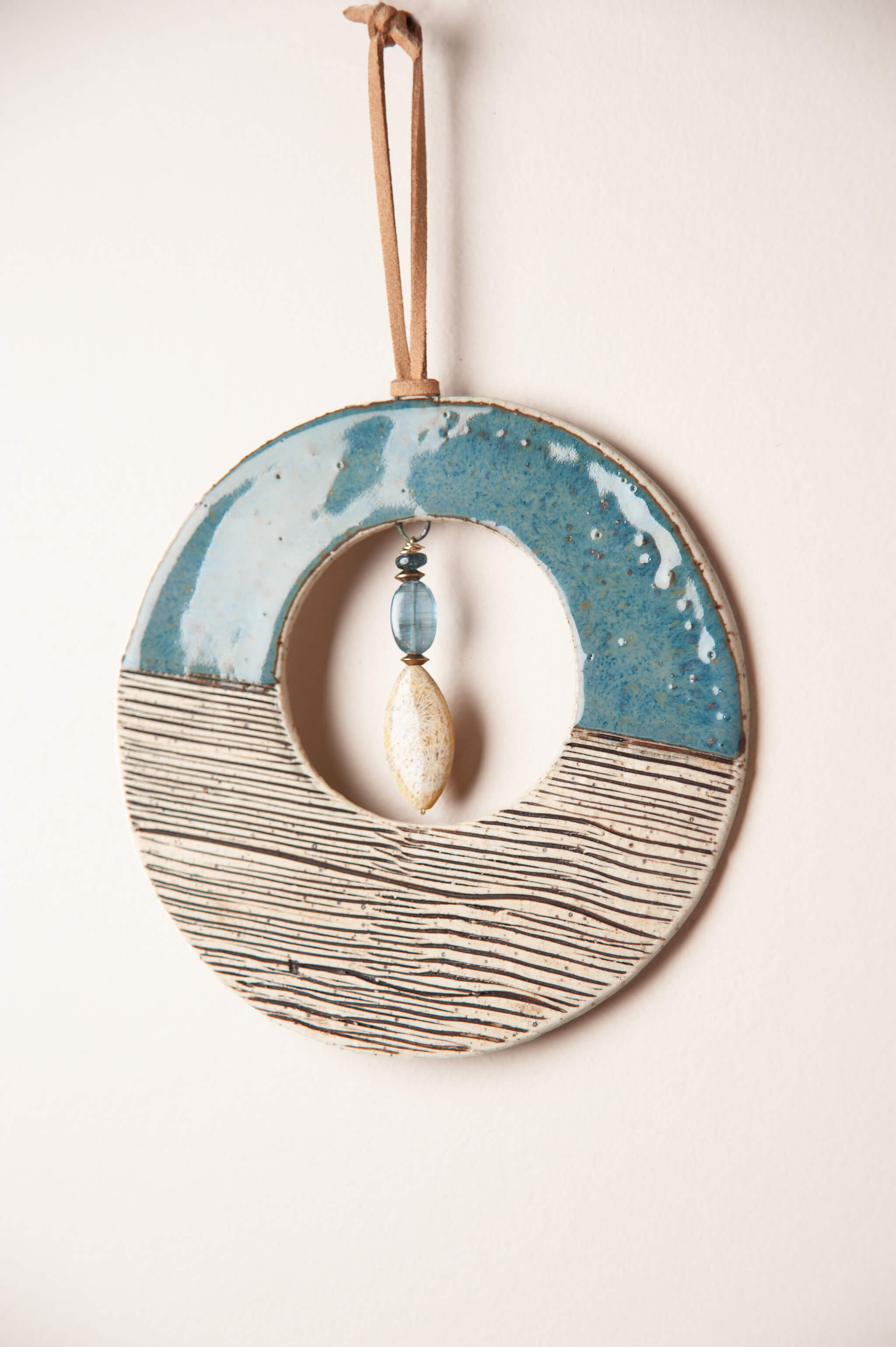 Detail of sea break blue glaze and hand pressed wave stripe pattern on small handmade ceramic wall hanging by Jester Swink, Santa Cruz Mountains California