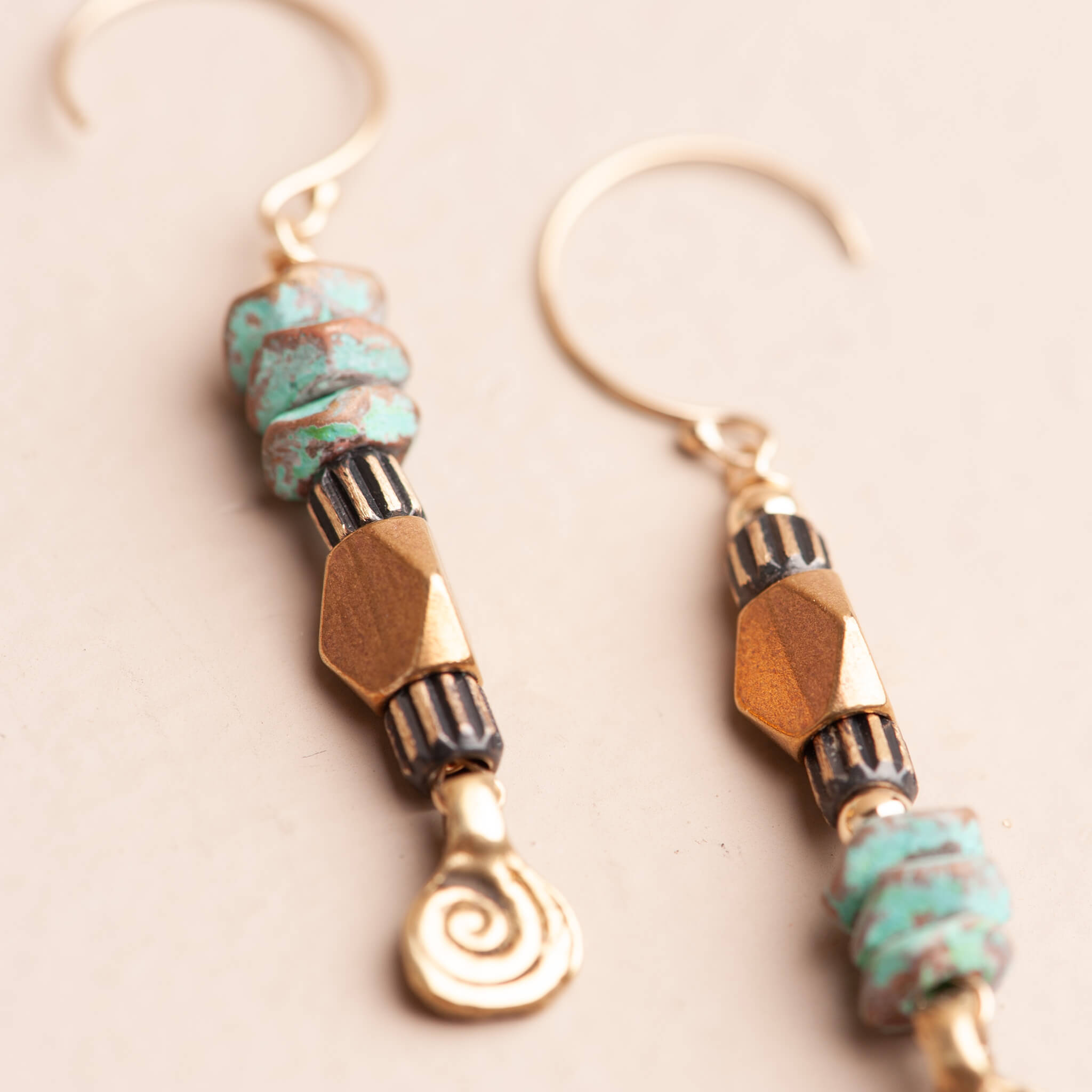Close-up detail of turquoise patina brass beads and spiral charm on handmade dangle earrings