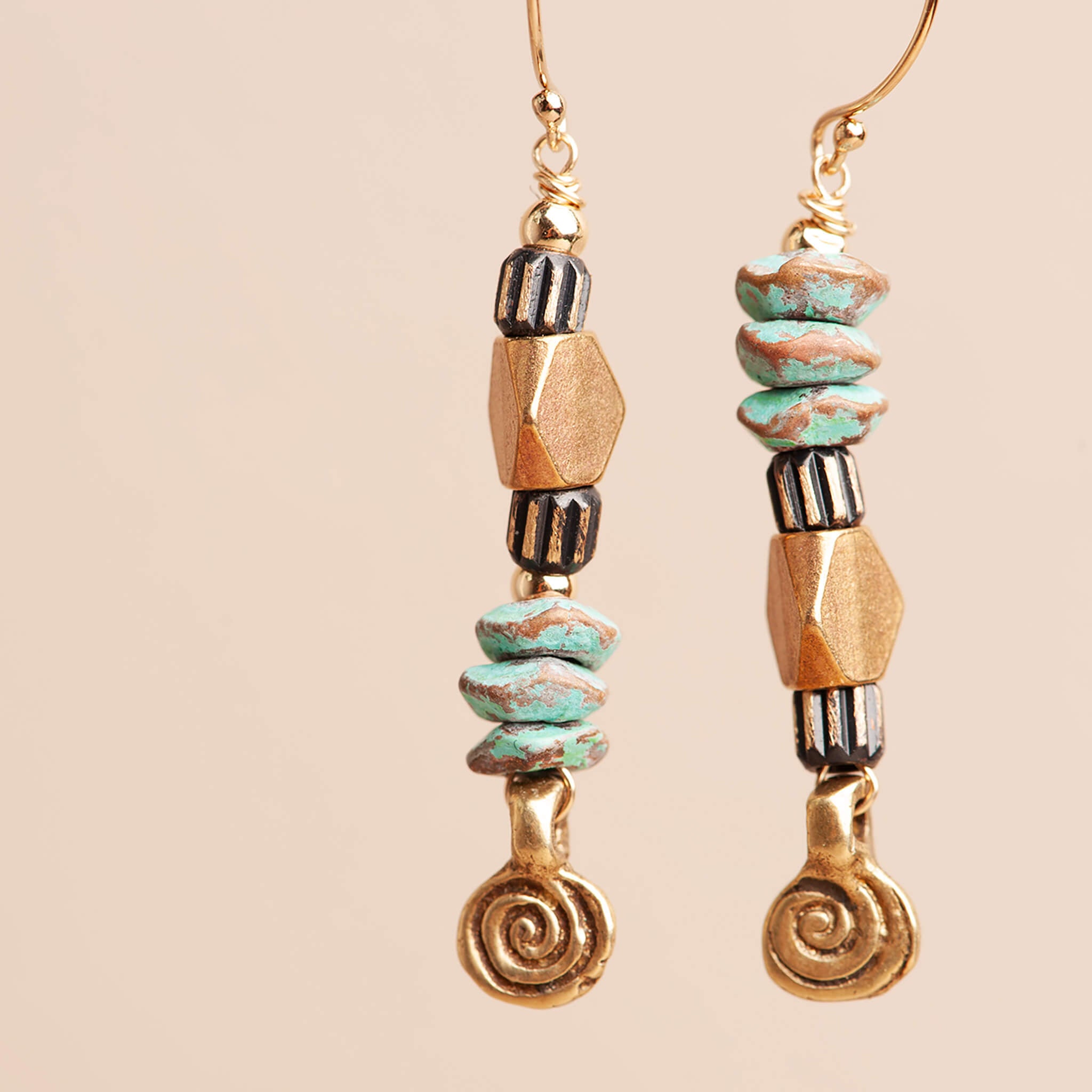 Asymmetrical turquoise patina brass spiral earrings photographed at an angle showing texture and movement