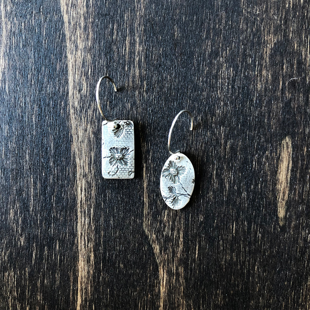 Pair of handcrafted sterling silver dangle earrings featuring an imprinted floral lace texture, with one pendant being rectangular and the other oval.
